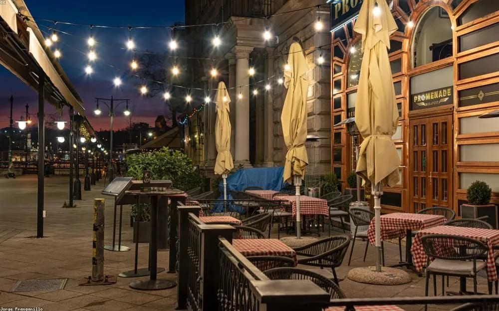 Tables set out on a restaurant terrace under string lights in the evening